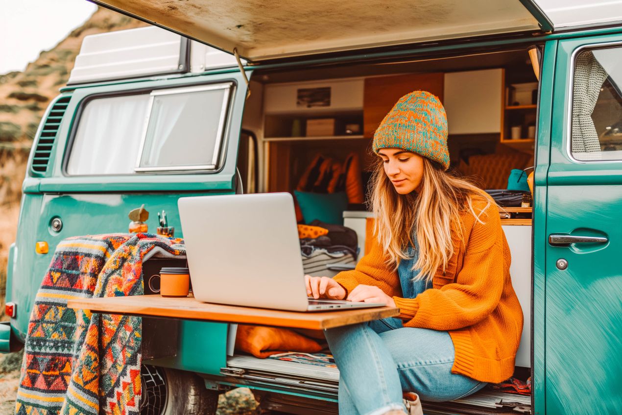 Junge Frau in einem Campervan mit Laptop, arbeitet flexibel und verbindet Job mit Reisen und Abenteuer.