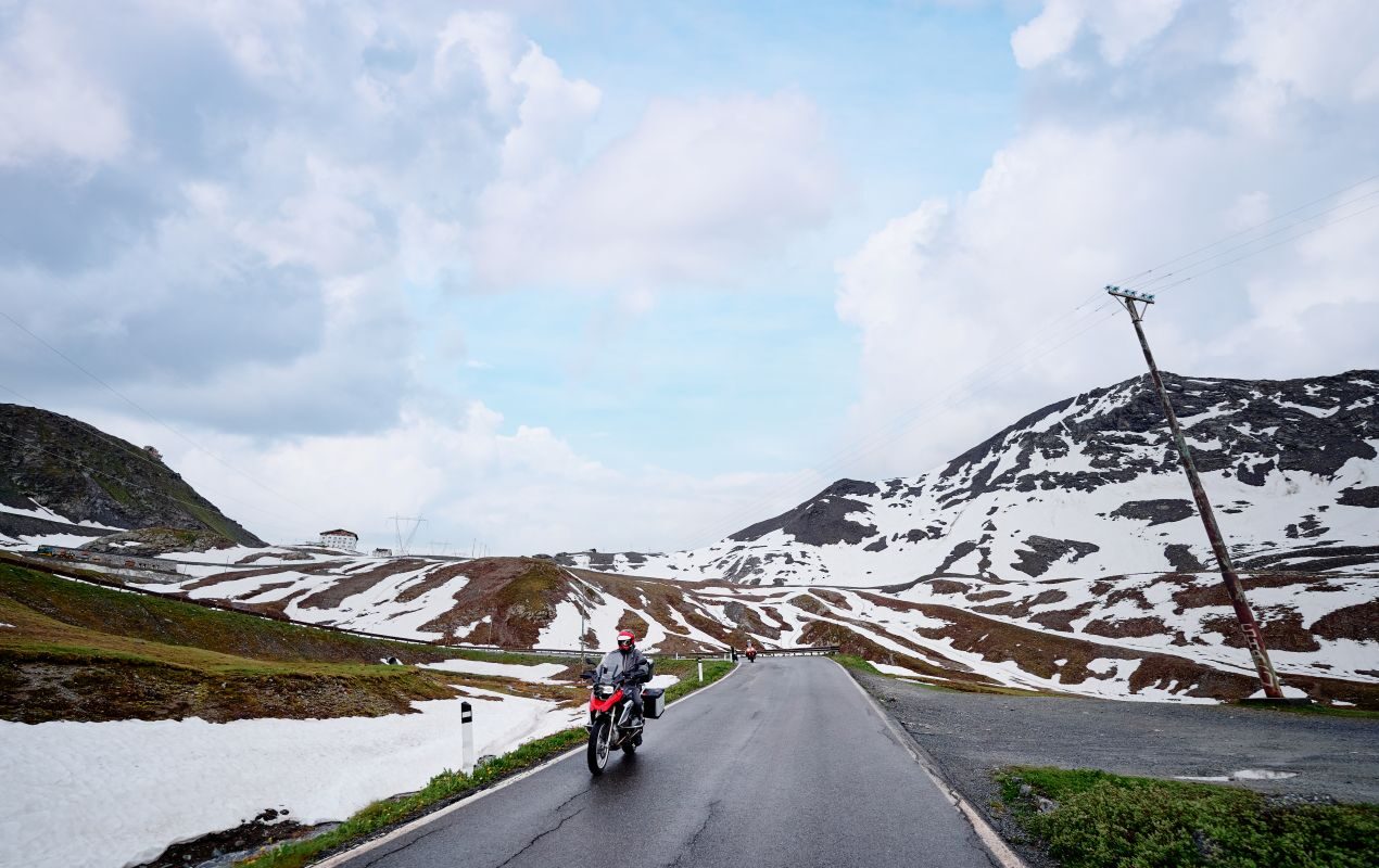 Motorradfahrer auf einer schneebedeckten Bergstraße in den Schweizer Alpen bei klarem Himmel