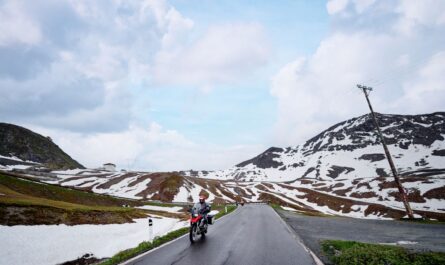 Motorradfahrer auf einer schneebedeckten Bergstraße in den Schweizer Alpen bei klarem Himmel