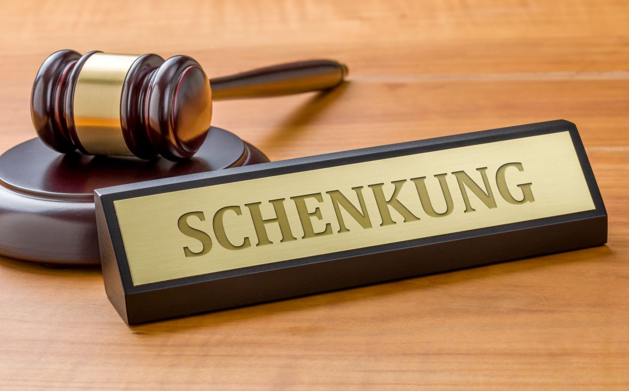 Nahaufnahme eines Richterhammers mit dem Schild „Schenkung“. Gesetzliche Regelungen und Steuerfragen im Erbrecht Würzburg.