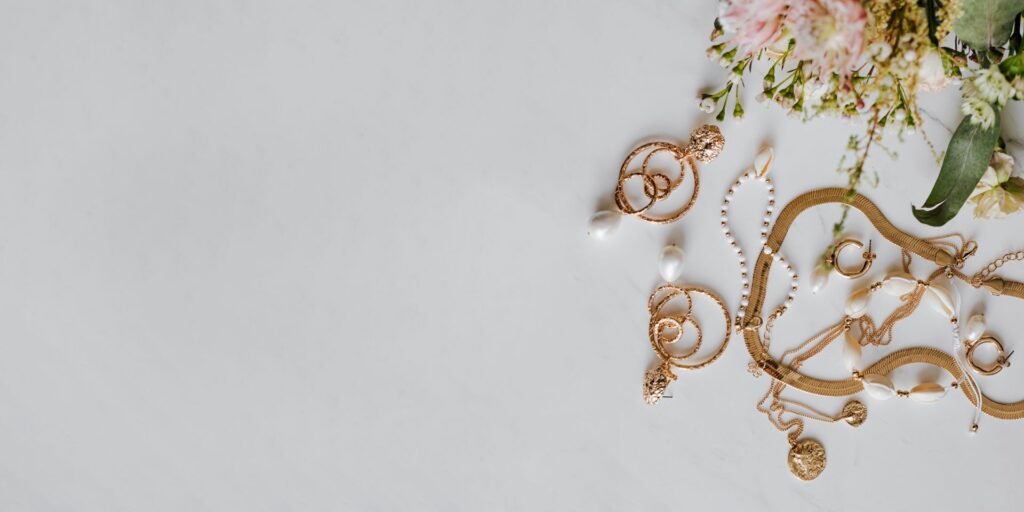 Goldschmuck mit Perlen wie von Bernd Wolf – flach gelegte Accessoires mit floralen Elementen auf hellem Untergrund